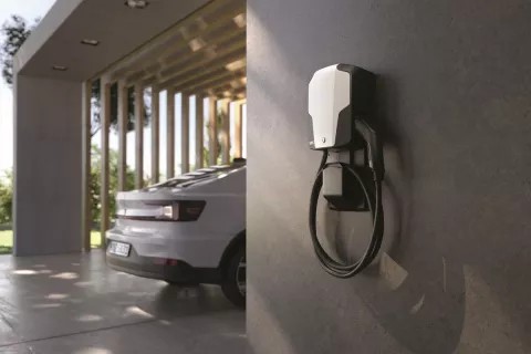 Eine Wallbox hängt an der Wand und im Hintergrund steht ein Elektroauto.